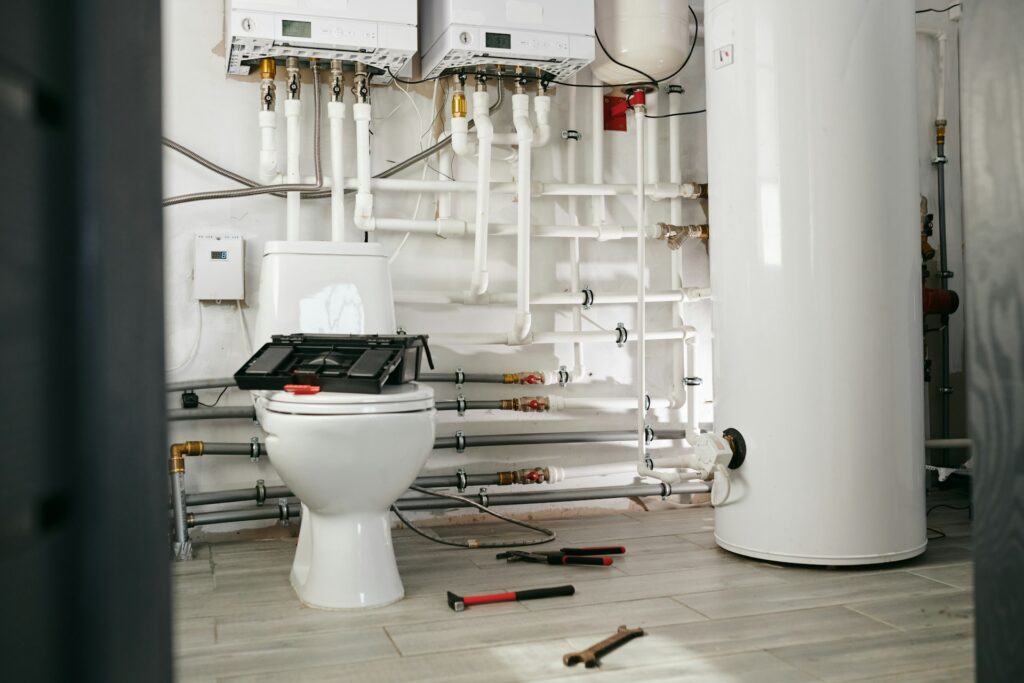 A bathroom containing a toilet, water heater, and plumbing pipes, designed for both utility and comfort.